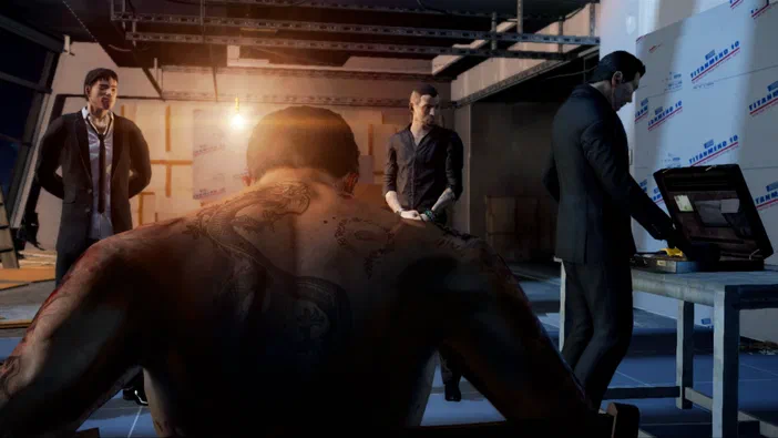 Capture d'écran du jeu Sleeping Dogs avec plusieurs personnages dans un intérieur sombre ; au premier plan on voit le dos tatoué d'un homme assis, deux autres hommes debout à gauche et l'un examinant une valise ouverte sur une table.