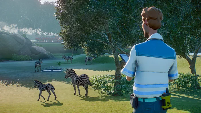 Dans le jeu vidéo Planet Zoo, un gardien vu par le dos observe une meute de zèbres évoluant dans leur enclos verdoyant parsemé d'arbres et de collines.