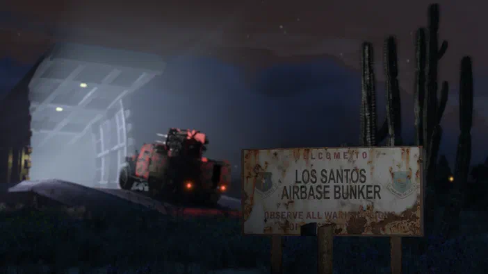 Panneau rustique indiquant Los Santos Airbase Bunker devant une bâtisse éclairée et des cactus sous un ciel de nuit dans Grand Theft Auto V