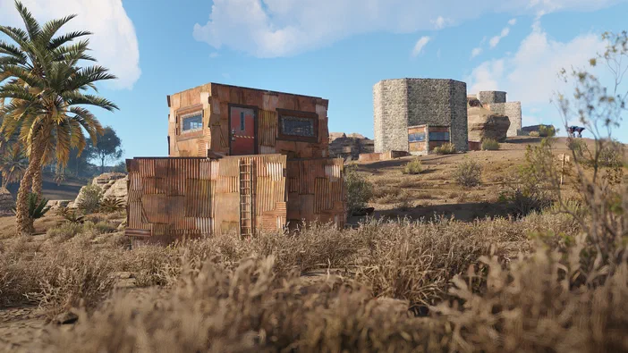 Capture d'écran du jeu Rust montrant une base en bois et métal rouillé construite dans un paysage désertique sec avec des collines arides à l'arrière-plan.