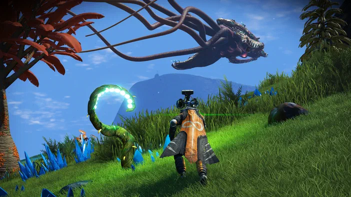 Dans No Man's Sky, un personnage en armure orange se tient sur une colline herbeuse parsemée de cristaux bleus sous deux créatures extraterrestres flottantes dans le ciel bleu.
