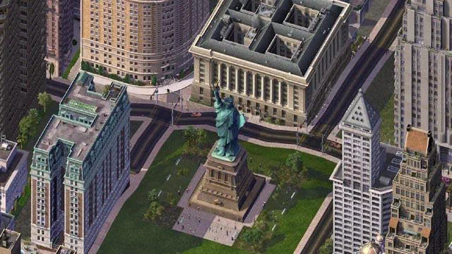 Capture d'écran du jeu vidéo SimCity 4 Deluxe présentant une vue aérienne d'un quartier urbain dense, où plusieurs immeubles hautes entourent un monument vert rappelant la Statue de la Liberté installé au centre d'une grande pelouse rectangulaire bordée par des routes et autres bâtiments.