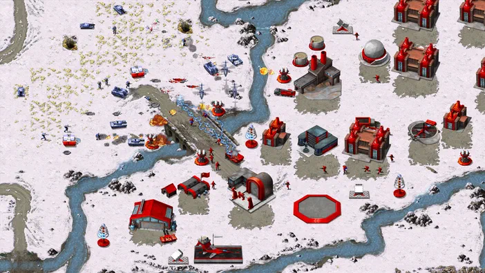 Capture d'écran du jeu de stratégie Command & Conquer™ Remastered Collection : un champ de bataille enneigé parsemé de rivières et de structures industrielles aux toits rouges avec des unités militaires en action.