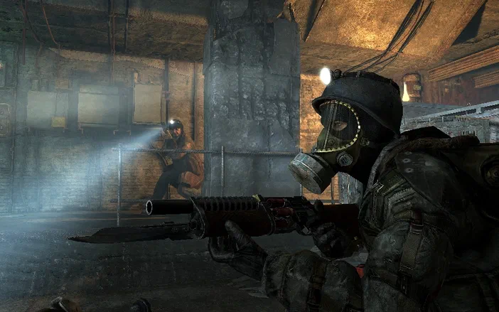 Dans un souterrain sombre d'un jeu vidéo post-apocalyptique, un personnage en masque à gaz tient une arme avec une lame déployée face à un autre individu éclairé par une lampe torche au loin.