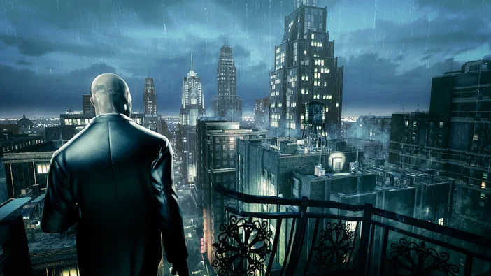 Personnage masculin à tête rasée vu par le dos en costume sombre se tenant sur une terrasse au-dessus d'une ville orageuse avec des immeubles illuminés dans Hitman: Absolution.