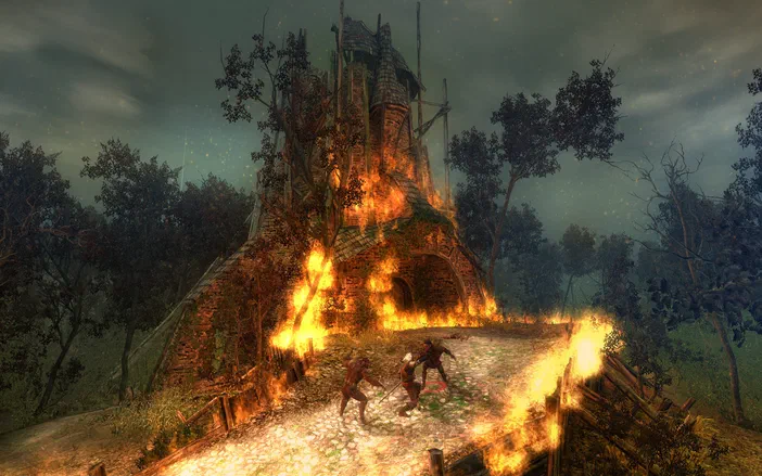 Dans The Witcher: Enhanced Edition, un personnage se bat contre deux ennemis devant un bâtiment en flammes dans un décor sombre et forestier.