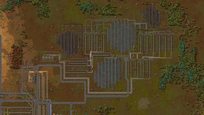 Vue de dessus d'une base complexe dans le jeu Factorio, montrant des rangées ordonnées d'usines et un réseau dense de tuyauteries reliant les bâtiments sur une carte.