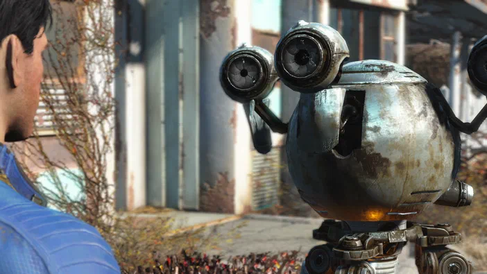 Dans le jeu Fallout 4, un personnage vu de dos observe un petit robot sphérique avec des antennes oculaires dans un environnement post-apocalyptique en ruine.
