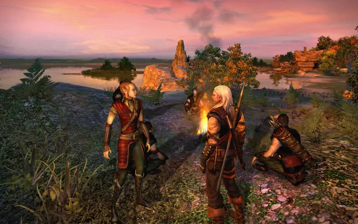 Capture d'écran de The Witcher: Enhanced Edition montrant Geralt et Triss autour d'un feu dans un paysage naturel au crépuscule.