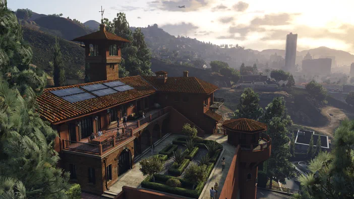 Vue aérienne d'une grande maison en briques avec un toit rouge, des panneaux solaires et un jardin géométrique où se trouvent plusieurs personnages dans Grand Theft Auto V.