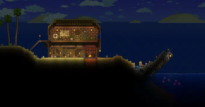 Capture d'écran du jeu vidéo Terraria montrant une maison en bois sur un plateau rocheux au bord de la mer la nuit.