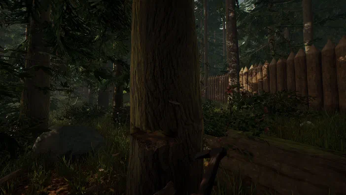 Capture d'écran du jeu vidéo The Forest montrant un environnement forestier avec de grands arbres, de l'herbe, une clôture en bois pointue à droite et un outil ressemblant à une hache au premier plan.