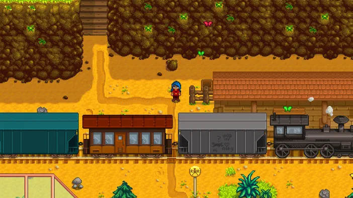 Capture d'écran du jeu Stardew Valley montrant un personnage aux cheveux bleus debout près de wagons de train et d'une locomotive noire dans un décor rural pixelisé.