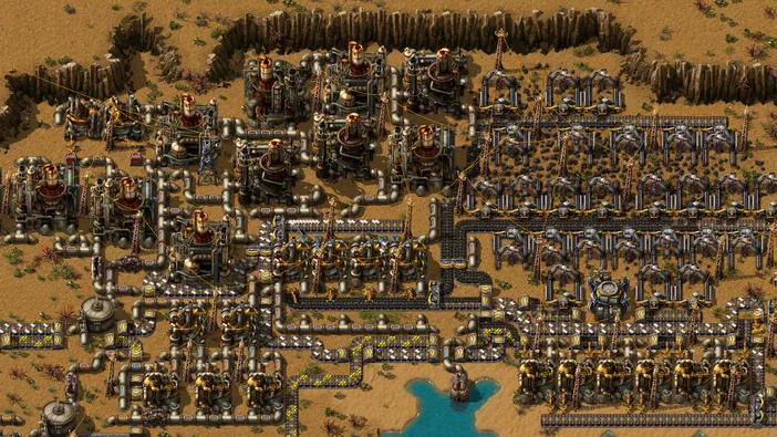 Vue de dessus d'une base industrielle complexe dans le jeu Factorio, remplie de structures mécaniques et de convoyeurs organisés sur un terrain désertique.