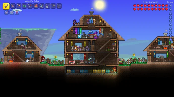 Capture d'écran du jeu vidéo Terraria montrant trois maisons en bois construites sur un terrain plat avec des personnages à l'intérieur et autour, ainsi qu'une base souterraine centrale sous une lune brillante dans le ciel bleu clair.