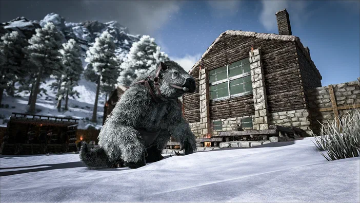 Une créature à fourrure grise équipée de sangles est assise sur un paysage enneigé avec des montagnes devant une base en bois dans le jeu vidéo ARK: Survival Evolved.