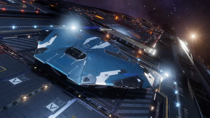 Un vaisseau spatial bleu et blanc futuriste est posé sur une vaste plateforme d'atterrissage aux multiples lumières dans la capture d'écran du jeu vidéo Elite Dangerous.