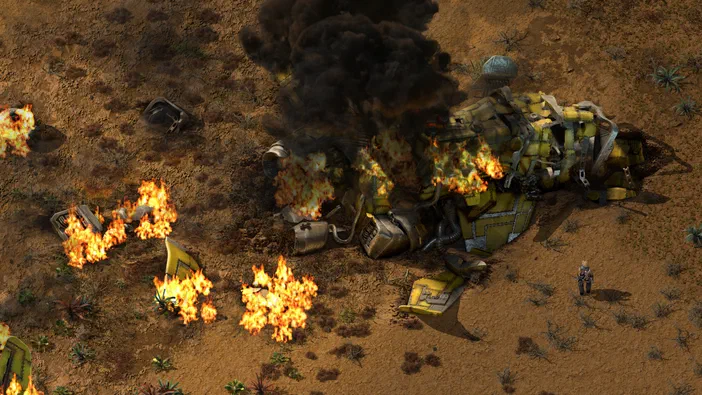 Dans le jeu Factorio, une vue de dessus montre un robot jaune en feu et fumant au sol aride, avec des débris brûlants autour.