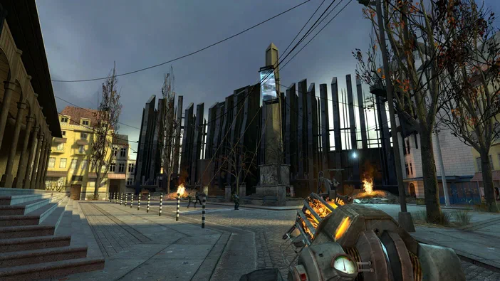 Capture d'écran du jeu vidéo Half-Life 2 montrant une rue urbaine aux bâtiments futuristes vus depuis le point de vue d'un personnage tenant une arme.