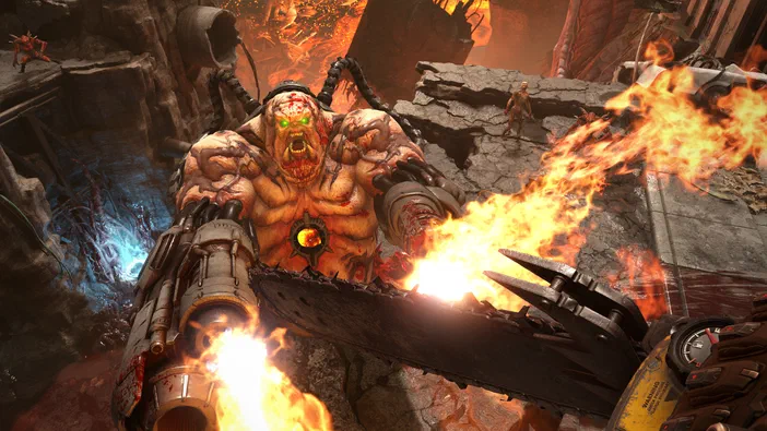Capture d'écran de DOOM Eternal montrant un démon géant aux yeux verts hurlant face à la chaîne de scie enflammée du joueur dans des ruines incendiées.