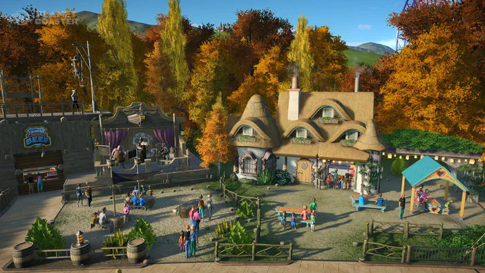 Scène de Planet Coaster montrant un parc aménagé avec des bâtiments en bois et herbeux, des visiteurs se promenant ou s'asseyant sur des bancs, entouré d'arbres aux couleurs automnales.