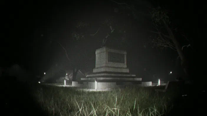 Capture d'écran du jeu Unknown Tapes montrant un monument funéraire en pierre au centre d'un cimetière sombre et brumeux la nuit.