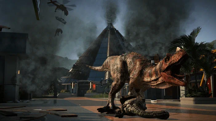 Dans Jurassic World Evolution, un T-Rex se tient sur le corps d'un dinosaure plus petit devant une tour en verre endommagée et des palmiers sous la pluie.