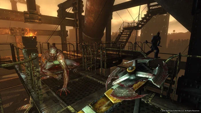 Capture d'écran de Fallout 3 montrant un mutant rampant sur une plateforme industrielle avec des structures métalliques et du feu en arrière-plan.