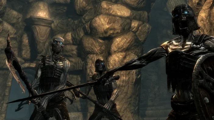 Capture d'écran de The Elder Scrolls V: Skyrim montrant trois personnages squelettiques armés dans une grotte rocheuse.