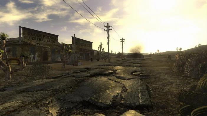 Vue de la ville désertique de Goodsprings dans Fallout: New Vegas avec des bâtiments en bois et un sol fissuré sous le soleil couchant.