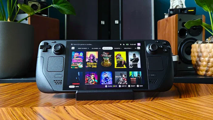 Steam Deck OLED affichant une interface de jeu avec des vignettes colorées sur un support en bois.