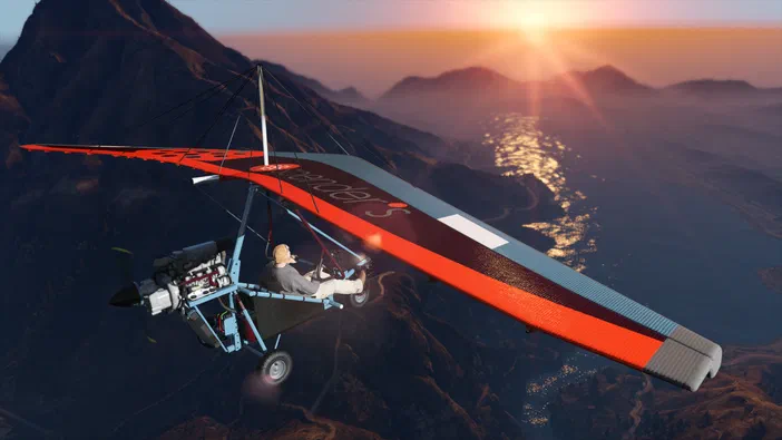 Capture d'écran de Grand Theft Auto V Legacy montrant un planeur motorisé rouge et bleu avec une personne à bord, survolant des montagnes au coucher du soleil.