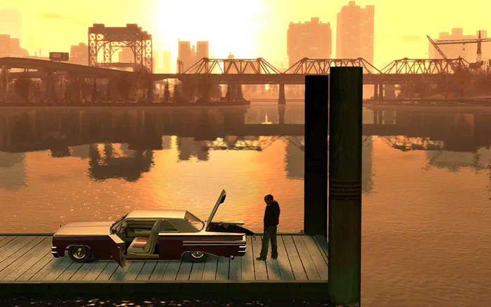 Dans Grand Theft Auto IV, un homme se tient sur une plateforme en bois avec sa voiture à côté d'un fleuve au coucher du soleil.