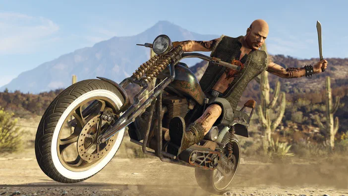 Dans Grand Theft Auto V Legacy, un personnage chauve à tatouages tient une machette en effectuant un wheelie sur sa moto dans un décor désertique.
