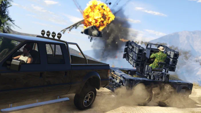 Dans Grand Theft Auto V, un camion noir tractant une plateforme de missiles est en mouvement sur une route poussiéreuse alors qu'un avion explose dans les airs au loin.