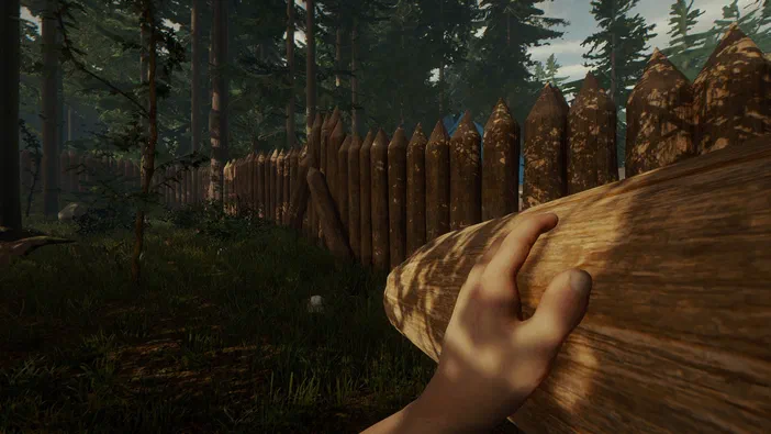 Dans le jeu vidéo The Forest, une main tient un tronc de bois devant une palissade en pointes dans une forêt dense.