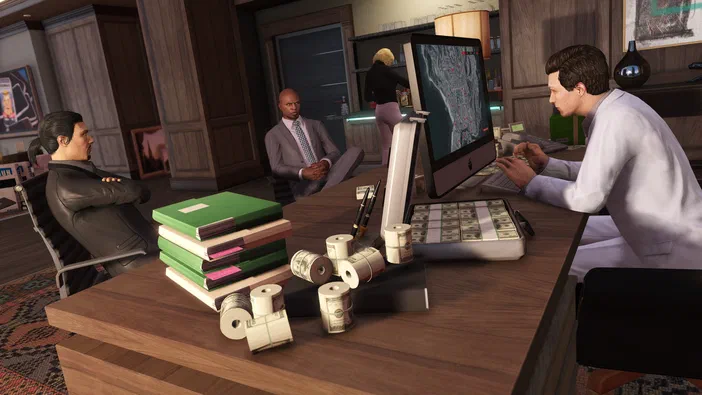 Dans Grand Theft Auto V Legacy, un bureau est encombré de liasses d'argent et de dossiers verts. Un homme en blouse blanche tape sur son clavier devant une carte géographique affichée à l'écran.