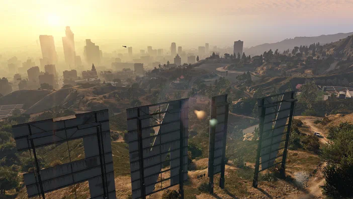 Vue panoramique d'une ville brumeuse au lever du soleil depuis une colline avec des panneaux publicitaires vides en premier plan dans Grand Theft Auto V.