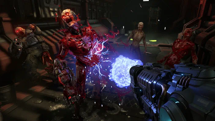 Dans DOOM Eternal, le joueur vise une créature démoniaque enflammée au centre d'une salle industrielle sombre entourée de plusieurs ennemis.
