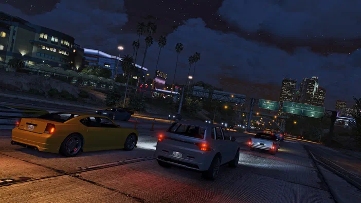 Capture d'écran de Grand Theft Auto V montrant plusieurs voitures sur une autoroute nocturne avec des gratte-ciels en arrière-plan.