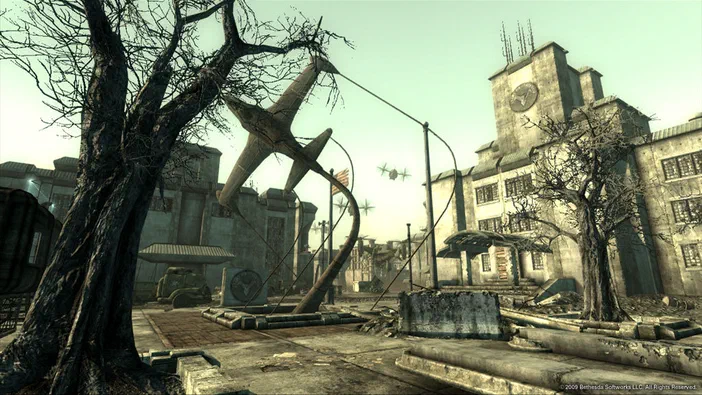Capture d'écran de Fallout 3 montrant une ville post-apocalyptique avec un avion en métal tordu accroché à des arbres et des bâtiments délabrés.