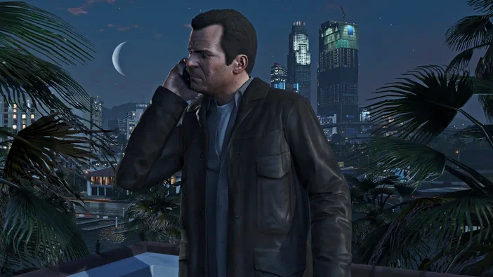 Dans Grand Theft Auto V Legacy, un homme en veste de cuir parle au téléphone sur une terrasse nocturne avec des palmiers et la ville illuminée à l'arrière-plan.