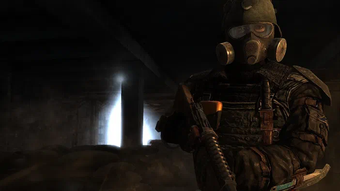 Dans le jeu vidéo Metro 2033, un personnage en tenue de protection avec masque à gaz et gilet tactique tient une arme dans un tunnel sombre éclairé par des fentes lumineuses.