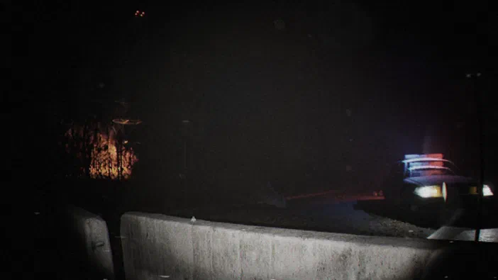 Capture d'écran du jeu vidéo Unknown Tapes montrant une voiture de police avec ses lumières clignotantes dans un environnement sombre.