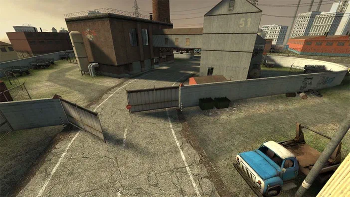 Vue aérienne d'une cour industrielle dans Counter-Strike: Source, avec des bâtiments en briques et une camionnette bleue.