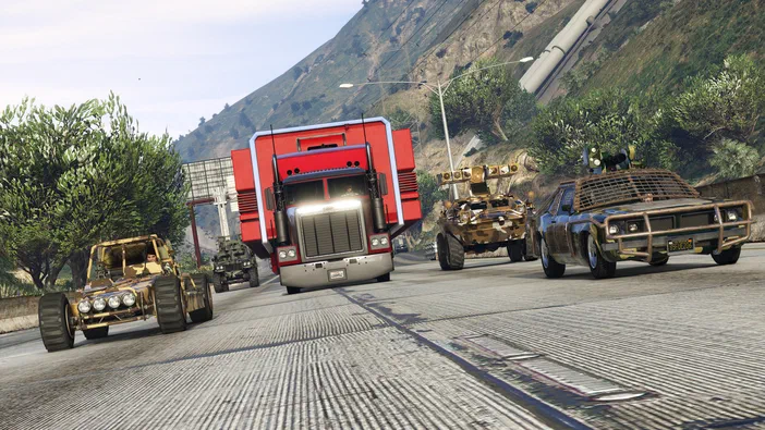 Dans Grand Theft Auto V Legacy, un camion rouge et plusieurs véhicules modifiés avancent sur une route en montagne.
