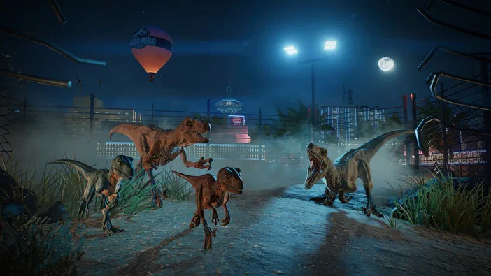 Dans Jurassic World Evolution 3, quatre dinosaures se tiennent sur une route nocturne devant un parc avec des lumières et un ballon.