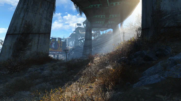 Vue sous un pont en béton dans Fallout 4 avec de la végétation et des ruines au loin.