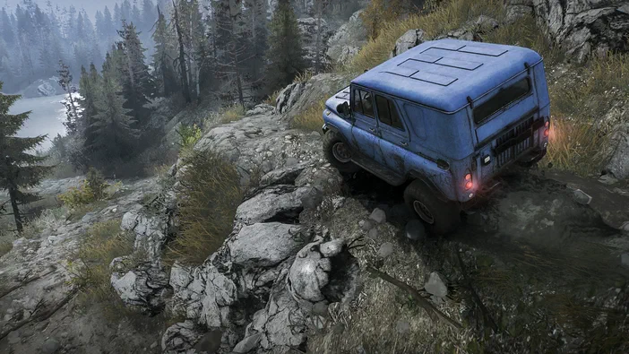 Capture de jeu vidéo MudRunner montrant un véhicule bleu sur une route rocailleuse en forêt.