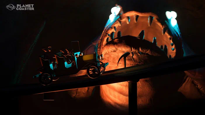 Dans le jeu Planet Coaster, un train de montagnes russes en forme d'auto des années 20 traverse la gueule ouverte d'un monstre géant éclairé par deux projecteurs bleus.